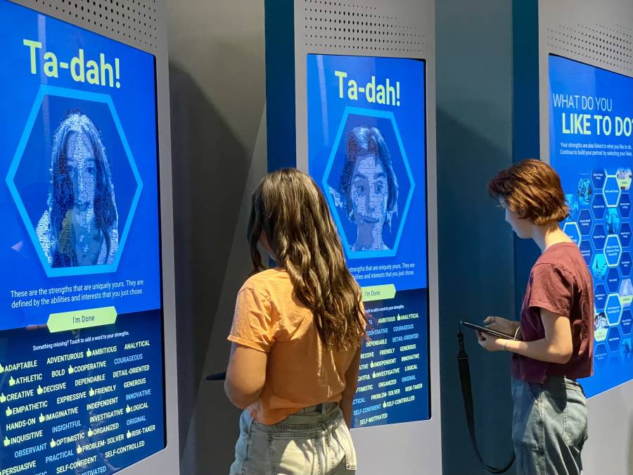 Two high school students stand in front of video screens that detail their career and personality interests